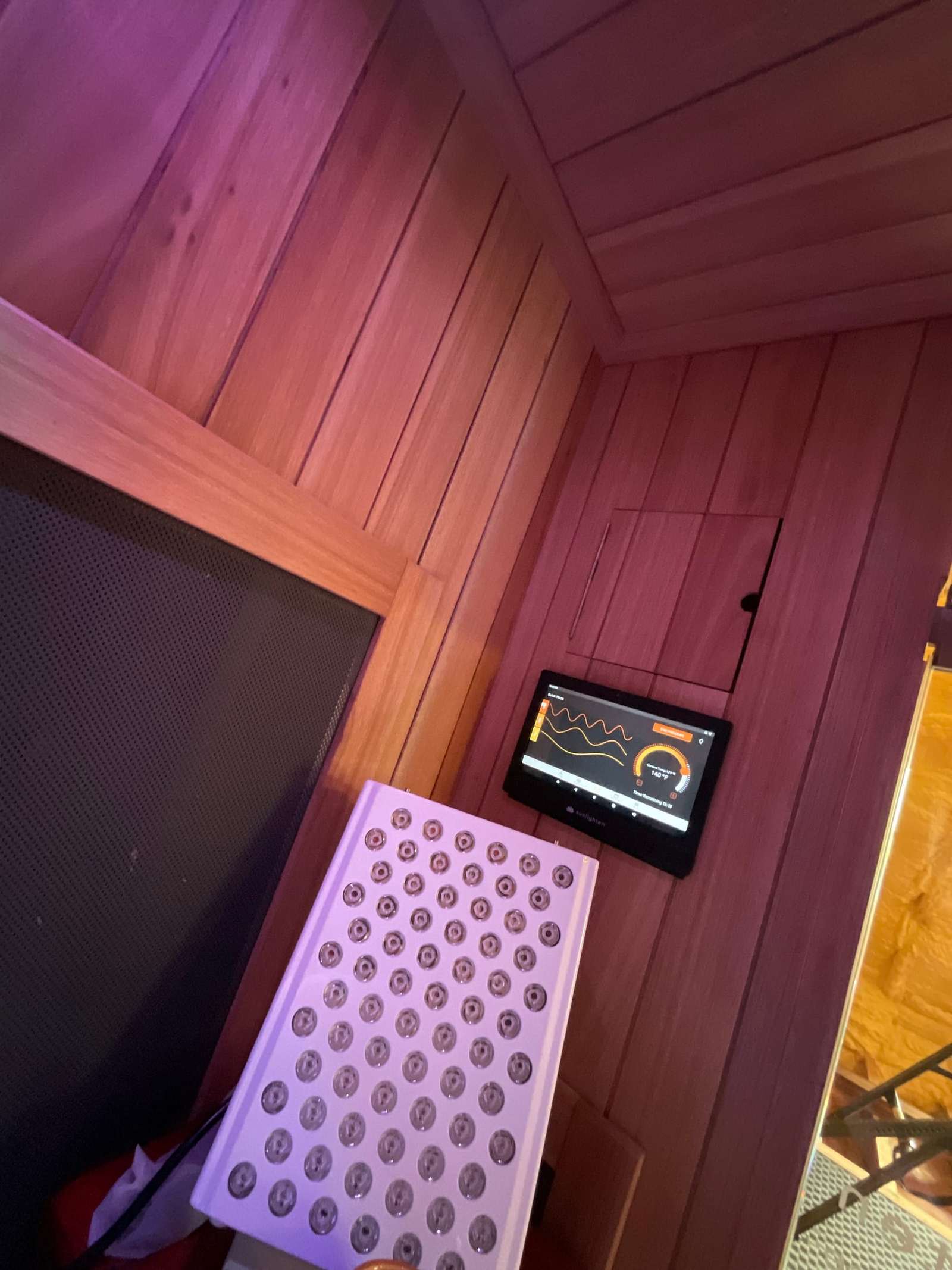Inside a cedar sauna, with a small control panel and a light panel on the wall.