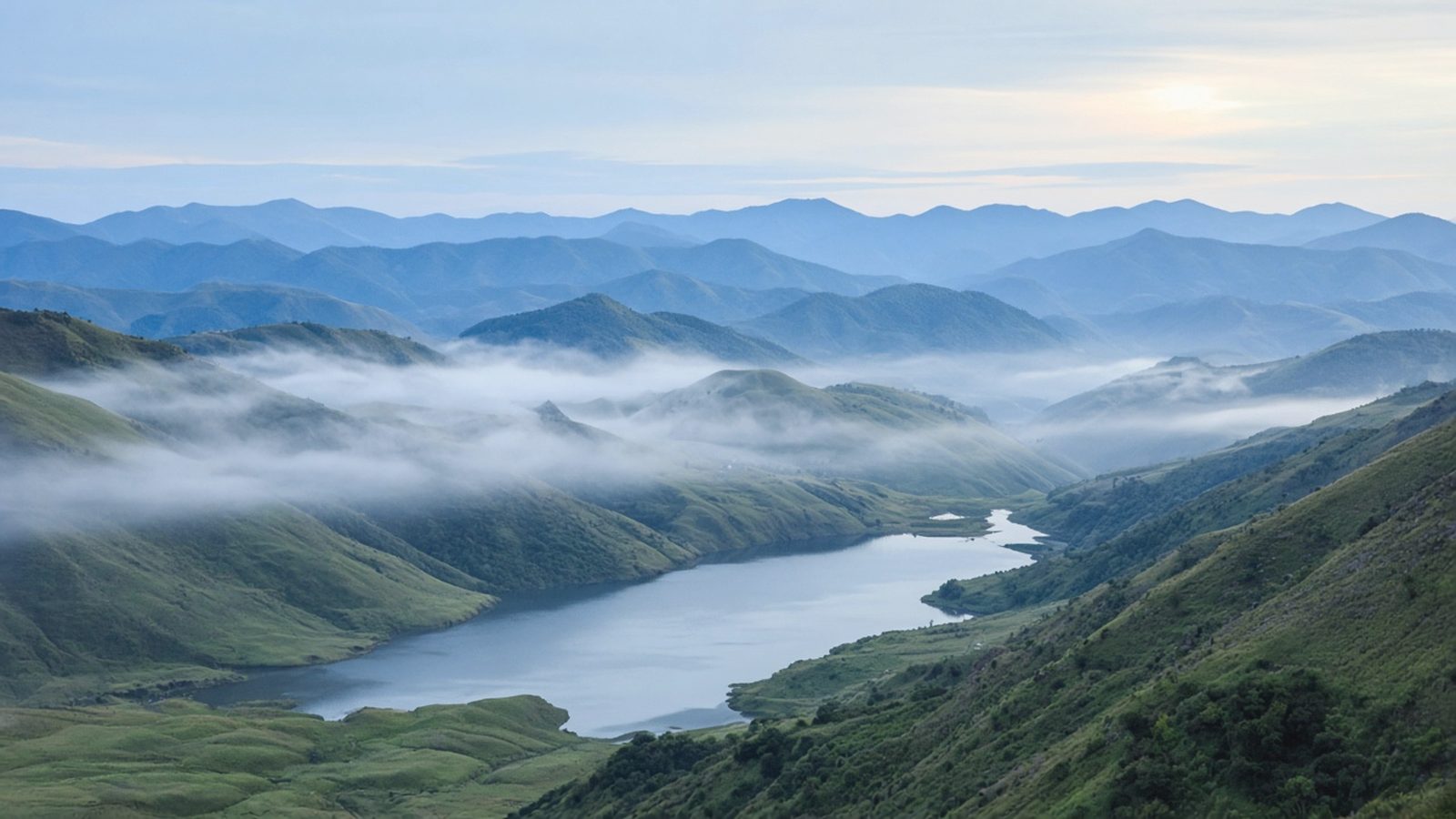 A wide mountain valley with a winding lake and morning mist.