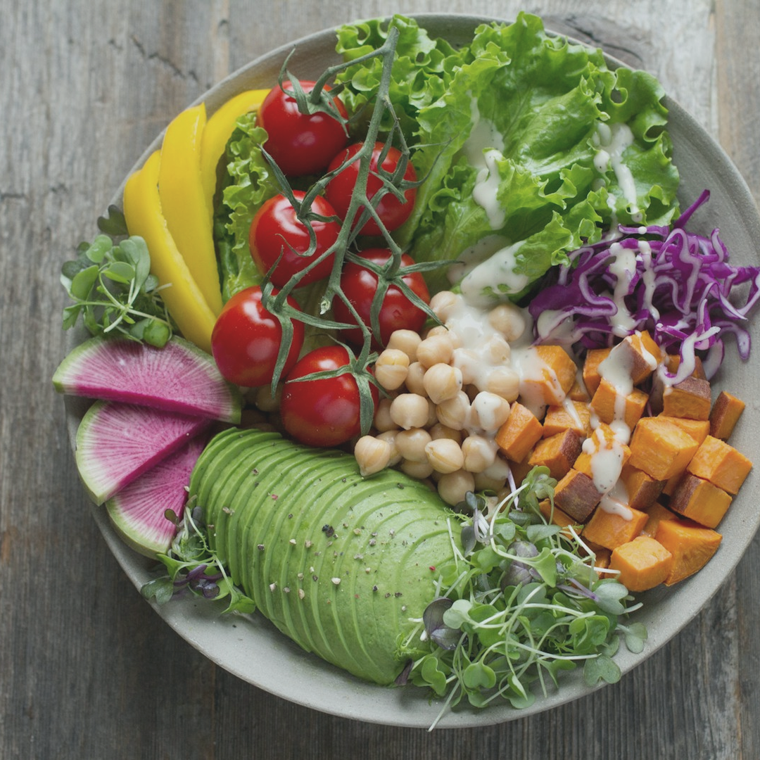 Overhead view of a colorful lunch bowl with greens, tomatoes, chickpeas, sweet potato and avocado